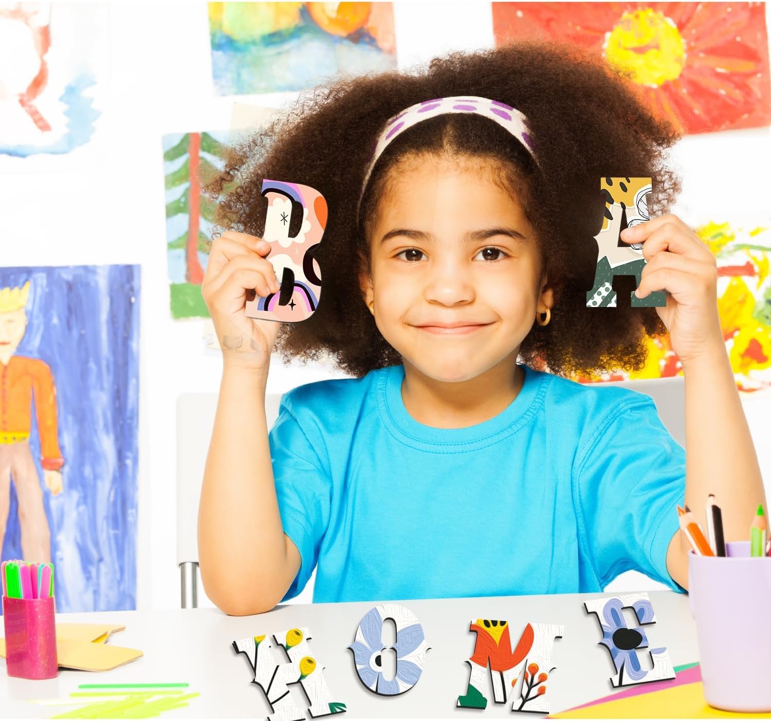 Child holding up letters in front of colorful artwork