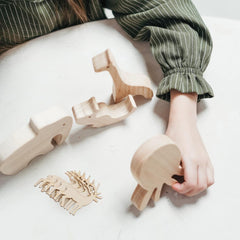 Wooden animal toys on a white surface with a person's hand interacting with one of them.