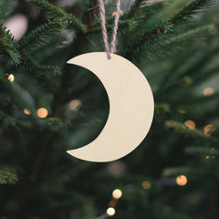Moon-shaped ornament hanging on a Christmas tree with blurred lights in the background
