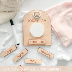 Dry erase baby milestones board with wooden markers on a soft fabric background