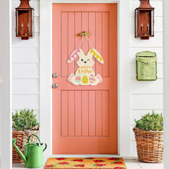 Pink door with Easter decorations, green watering can, and plants on a white wall.