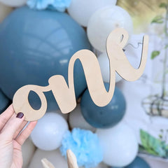 Wooden 'one' decoration held in front of blue and white balloons