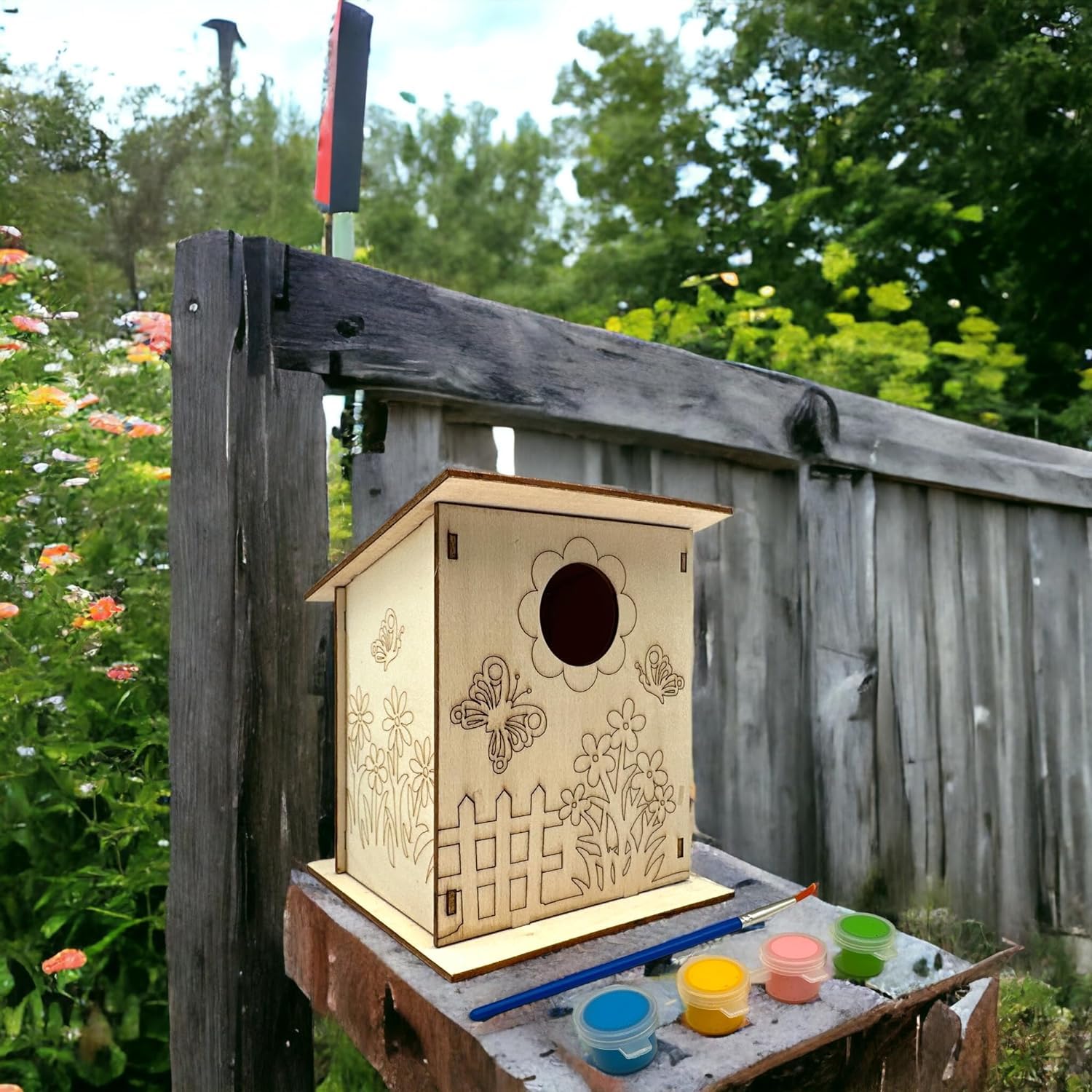 Wooden birdhouse with floral designs on a wooden stand outdoors.