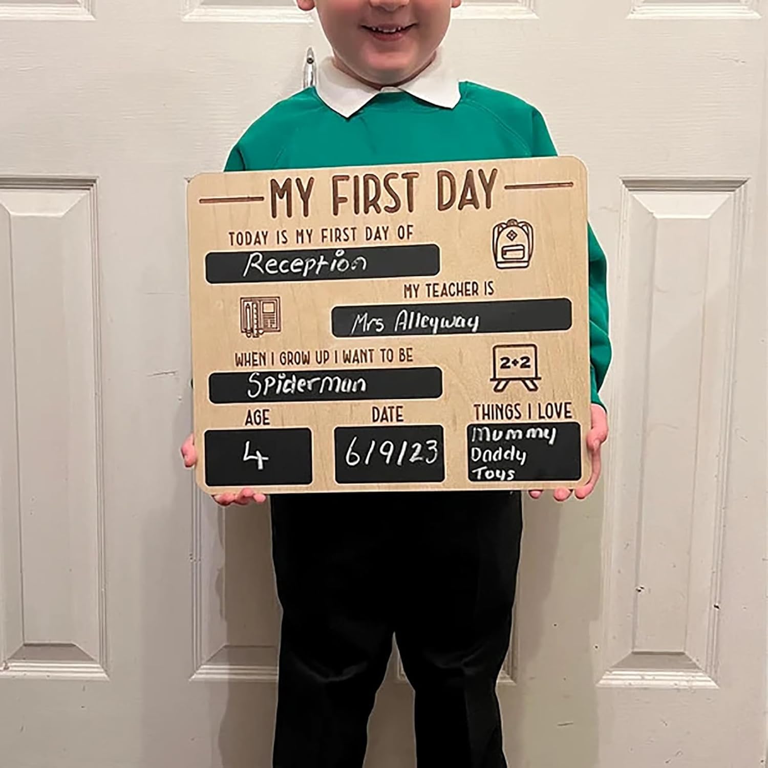 Child holding a 'My First Day' sign in front of a white door