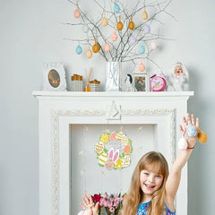 Child holding a small Easter decoration in front of a decorated fireplace with Easter eggs on branches.