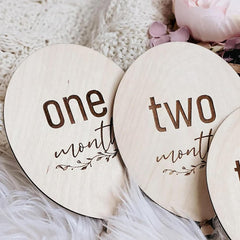 Wooden circular markers with 'one month' and 'two months' text on a soft surface.