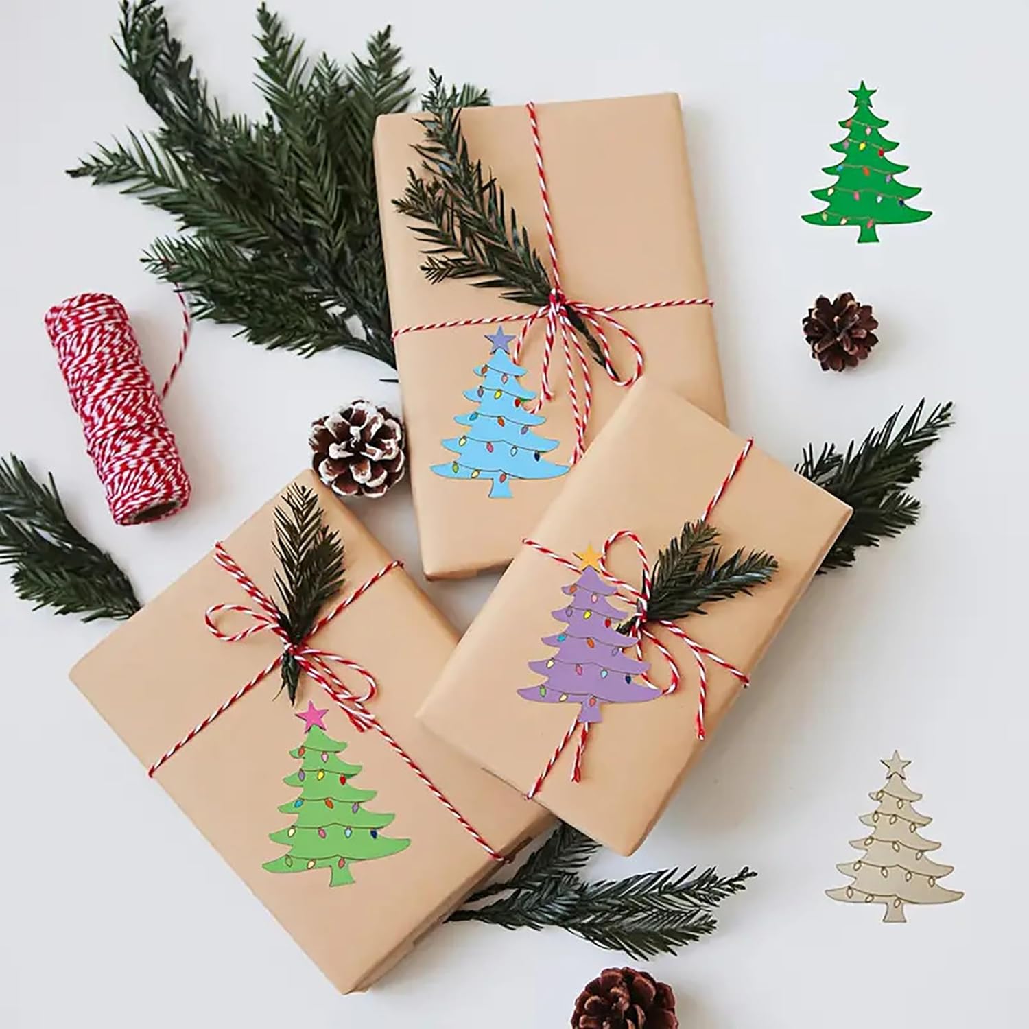 Three wrapped gifts with decorative tree stickers on a white background with pine branches and cones.