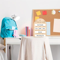 Teal backpack on a desk with a cork board displaying a 'First Day of 1st Grade' sign.
