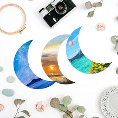 Colorful crescent moon-shaped cards with scenic designs on a white surface with decorative elements.