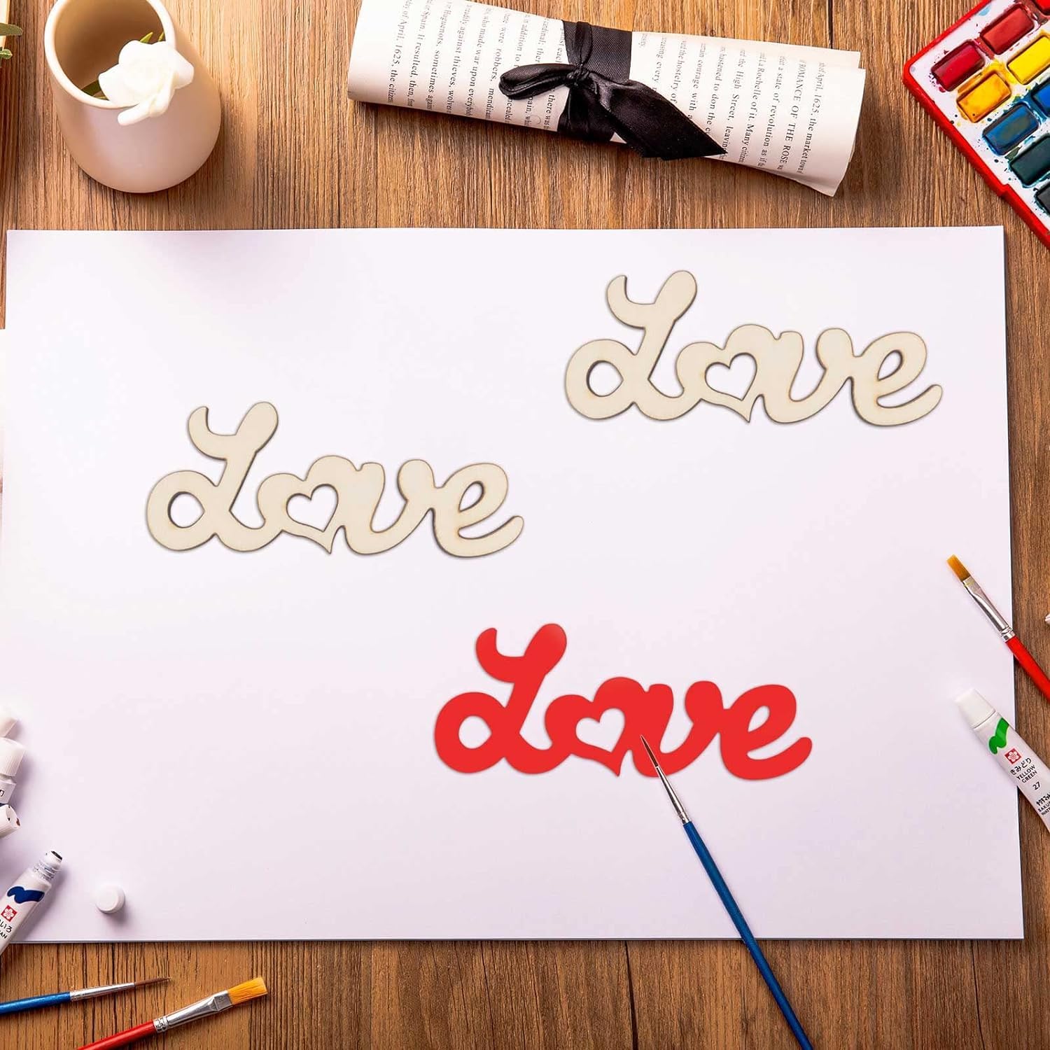 Wooden 'love' cutouts in different colors on a white sheet of paper with art supplies around.