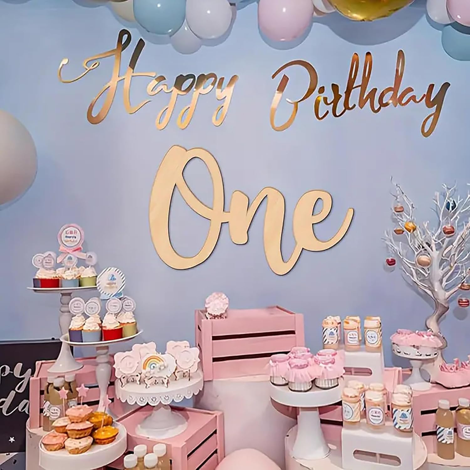 Birthday party setup with 'Happy Birthday One' sign, pink decorations, and various treats on a blue wall.