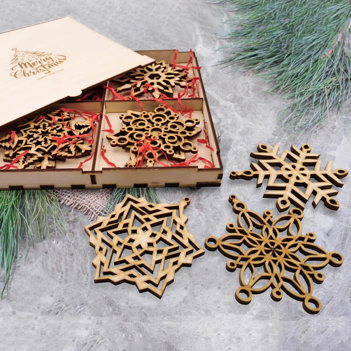 Wooden snowflake ornaments with a 'Merry Christmas' box on a textured surface with greenery.
