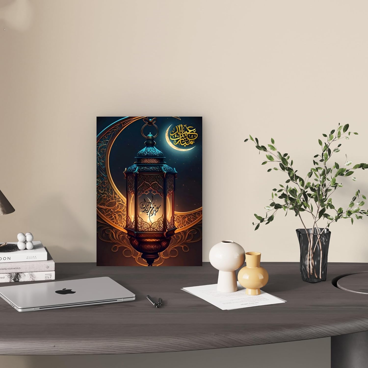 Decorative wall art of a lantern with Arabic text on a desk with a laptop and books.