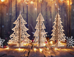 Three decorative Christmas trees with intricate cut-out designs on a wooden surface with a blurred festive background.