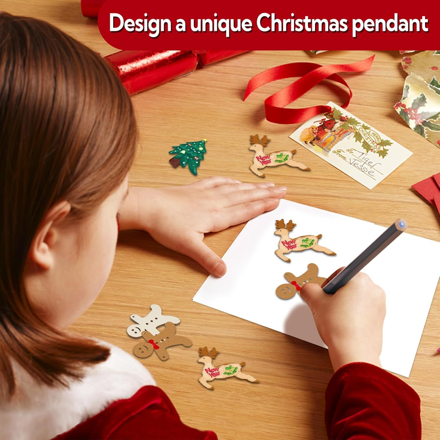 Child drawing a Christmas pendant on paper with decorative items on a table.