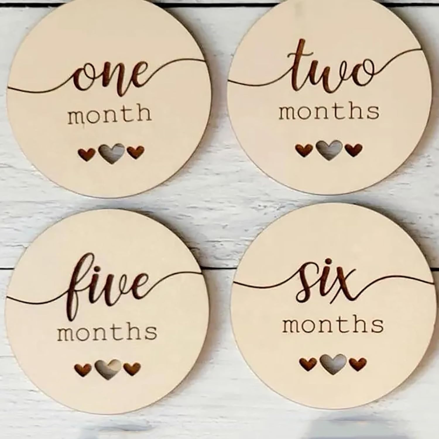 Four wooden discs with milestone labels for a baby's first year on a light wooden background.