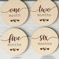 Four wooden discs with milestone labels for a baby's first year on a light wooden background.
