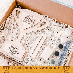 Wooden 'best dad in the world' award with paint supplies in a box, labeled 'Father's Day Award DIY'.