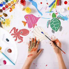 Children's hands painting sea creature drawings on a white surface with art supplies.