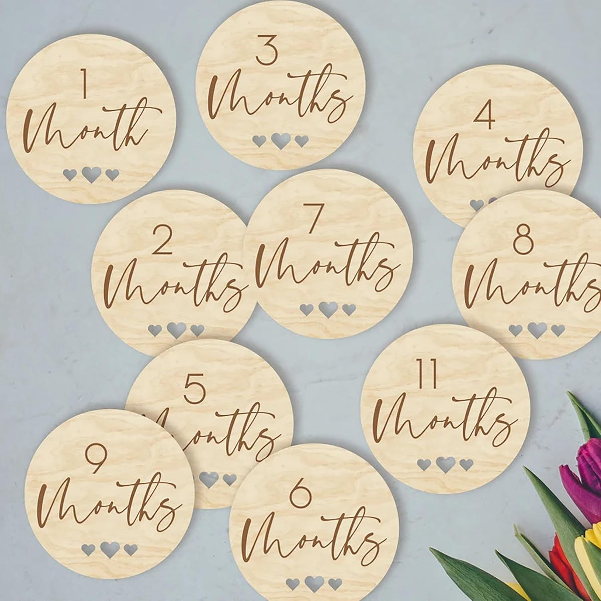 Wooden milestone discs for baby photoshoots with months printed on them against a light blue background.