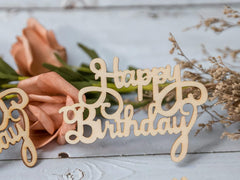 Wooden 'Happy Birthday' decoration with flowers on a light wooden surface
