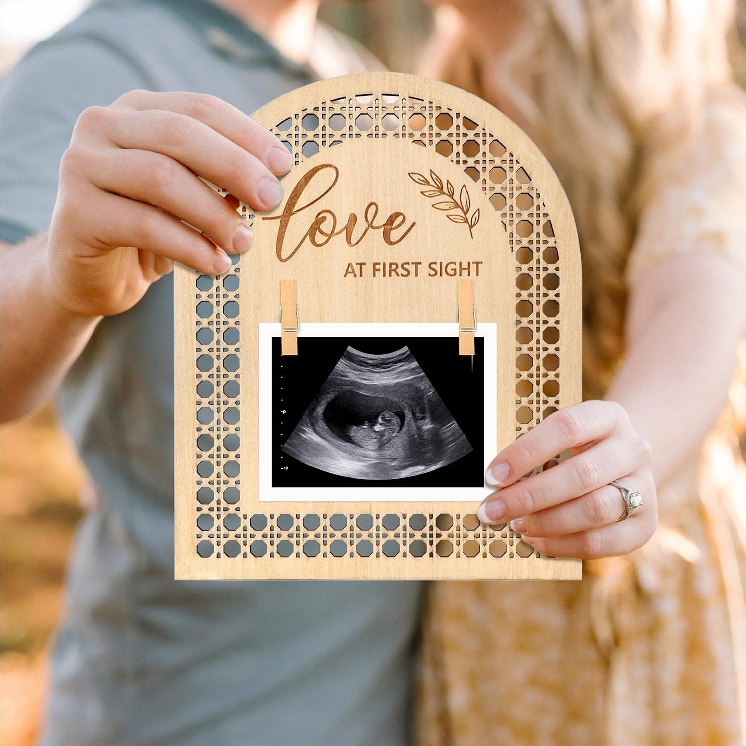 Wooden frame with 'Love at First Sight' text holding an ultrasound photo, held by a person.