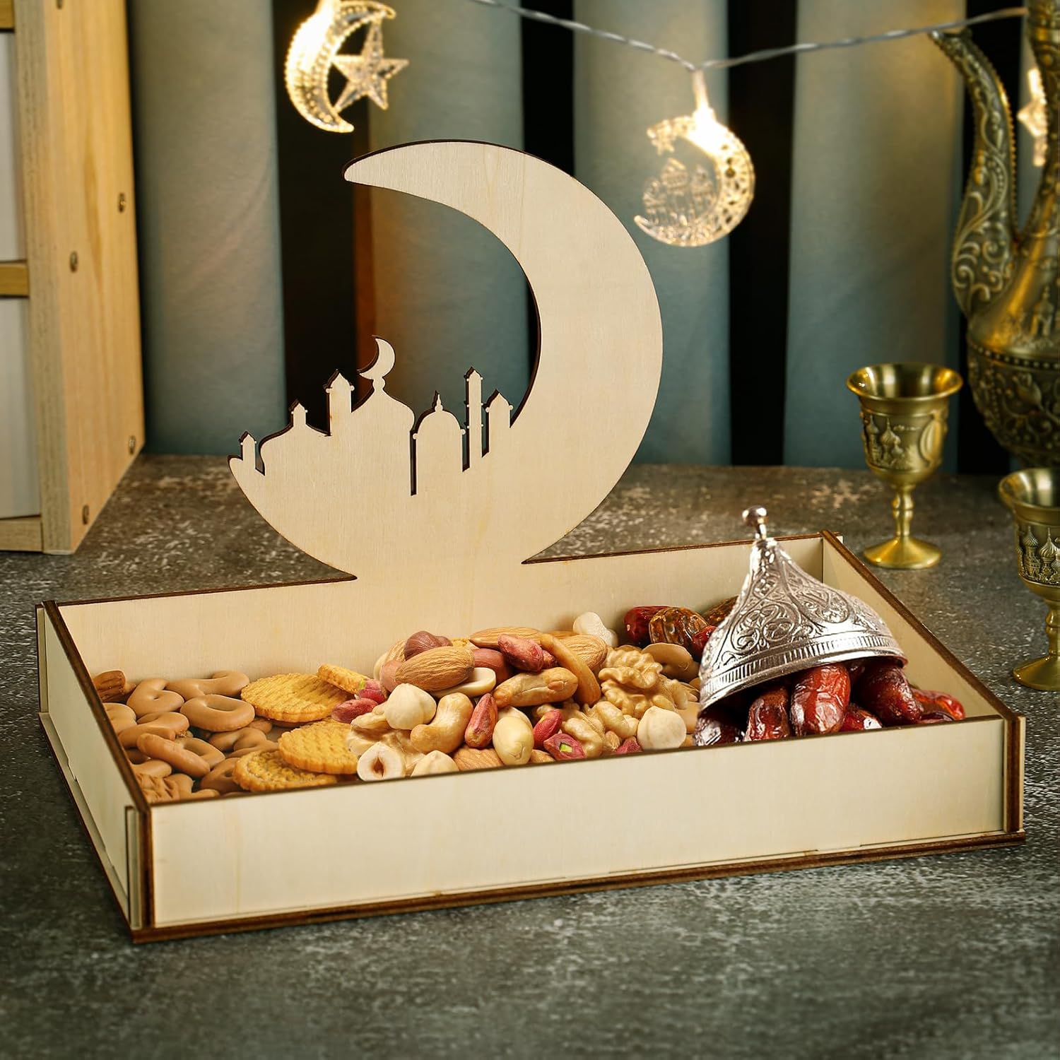 Box with a moon and cityscape design filled with snacks, placed on a reflective surface with decorative lights in the background.