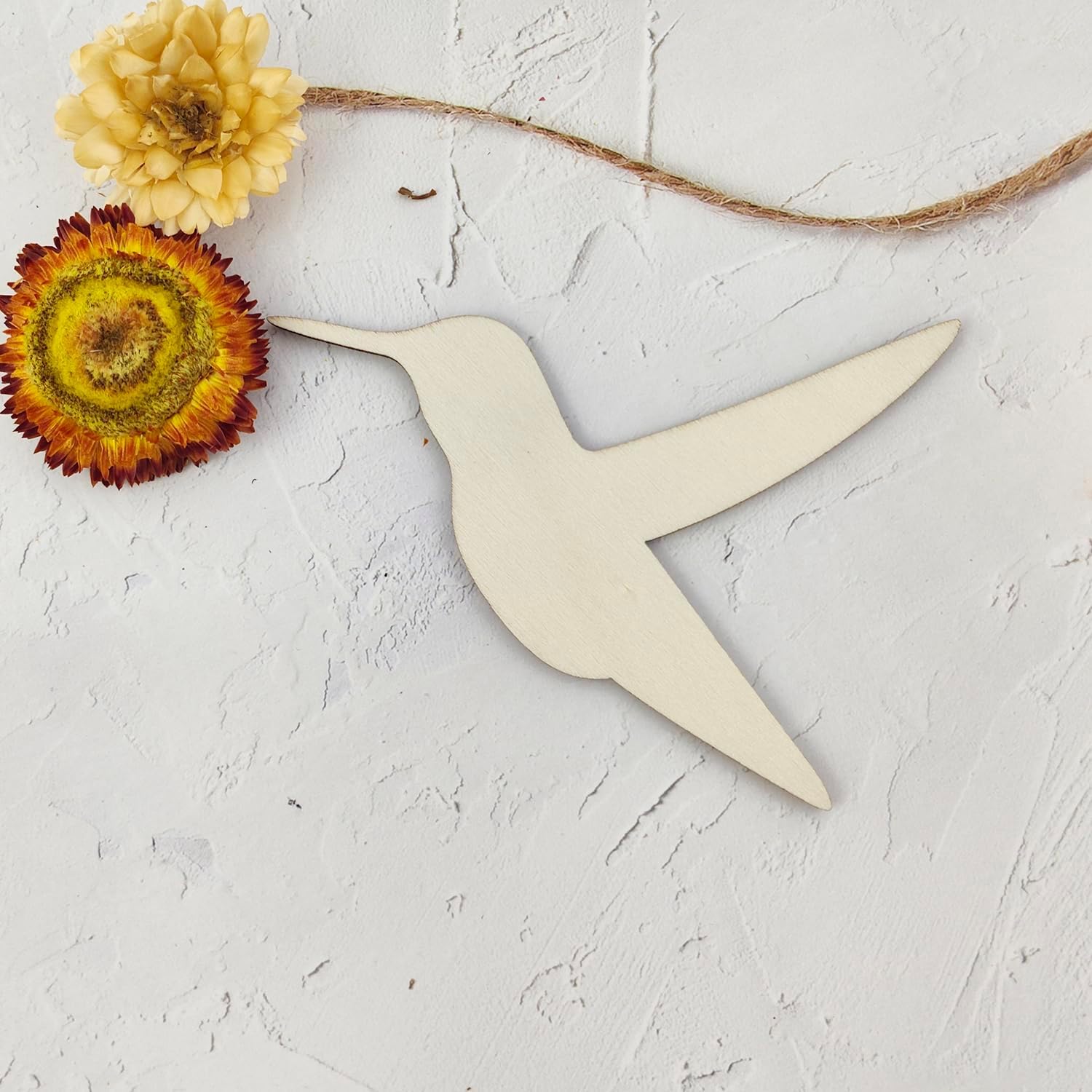 Wooden hummingbird-shaped cutting board on a textured white surface with two dried flowers.