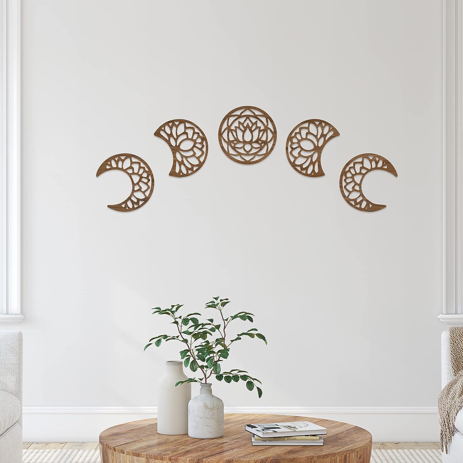 Decorative wall art of moon phases on a white wall with a wooden table and plant in the foreground.