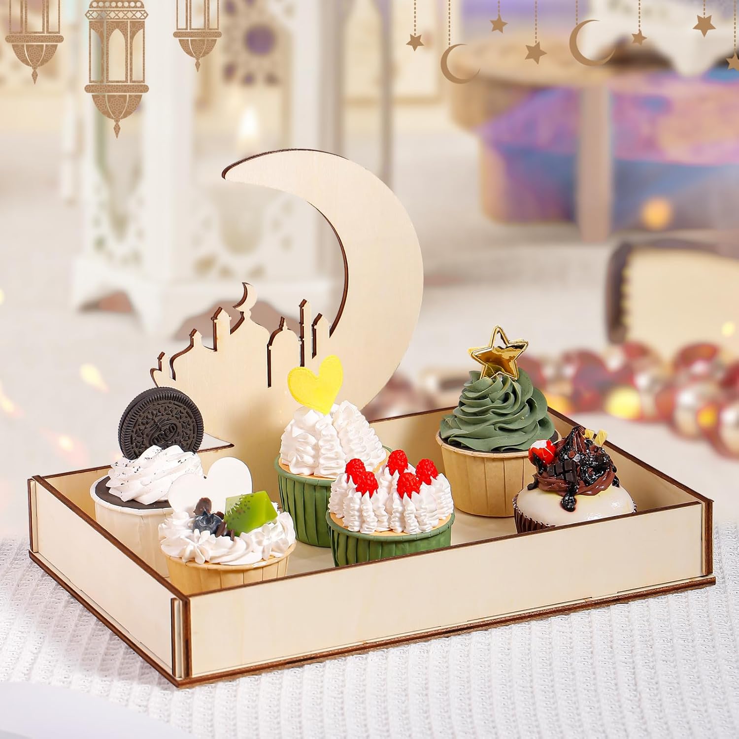 Decorative set with small cakes and a moon-shaped stand on a reflective surface.