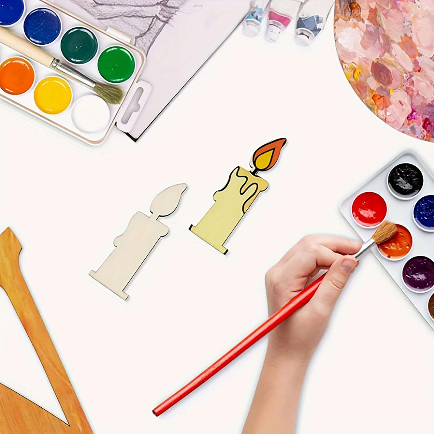 Artistic activity with watercolor paints, brushes, and candle-shaped objects on a white surface.
