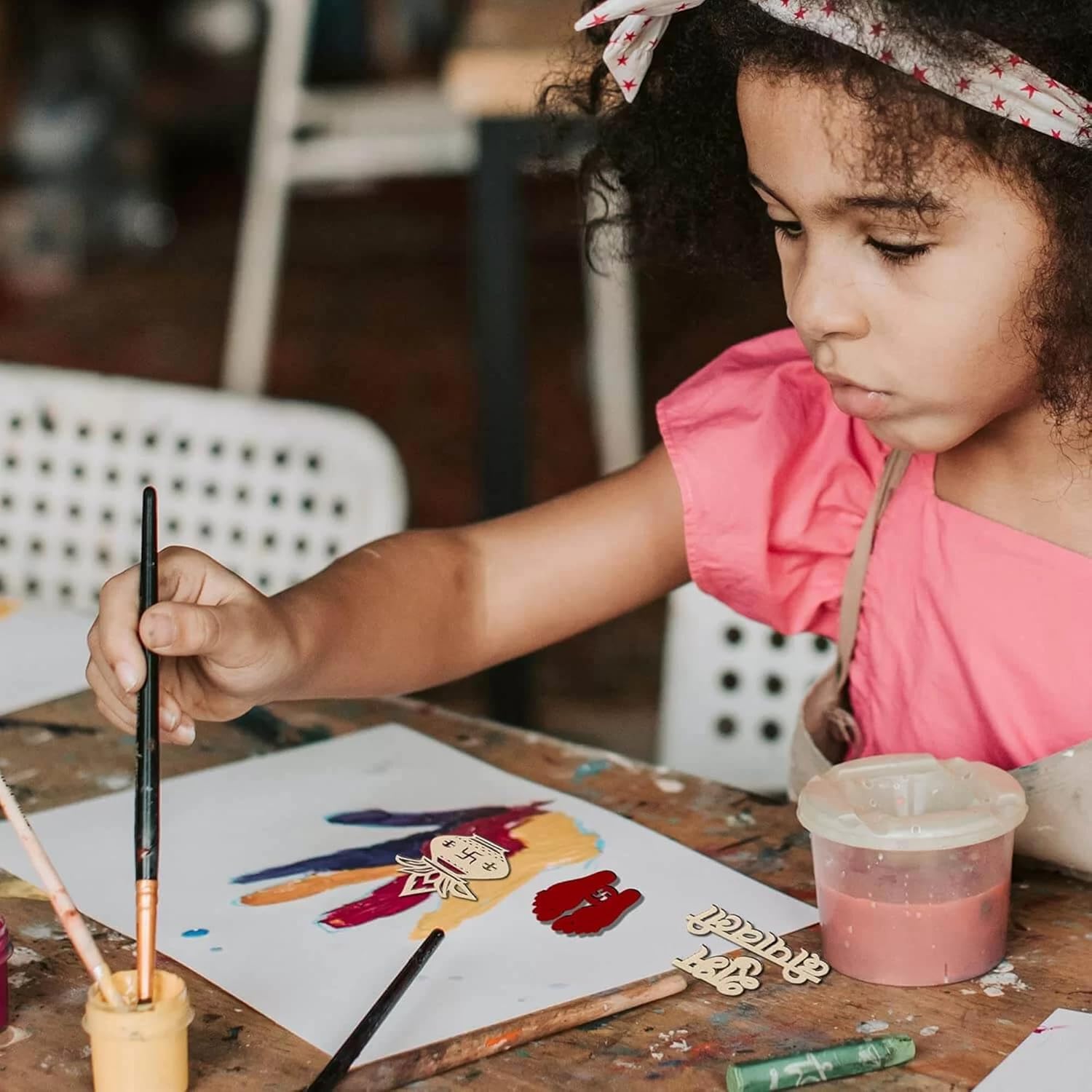 Child painting a colorful design on paper with a brush at a table.