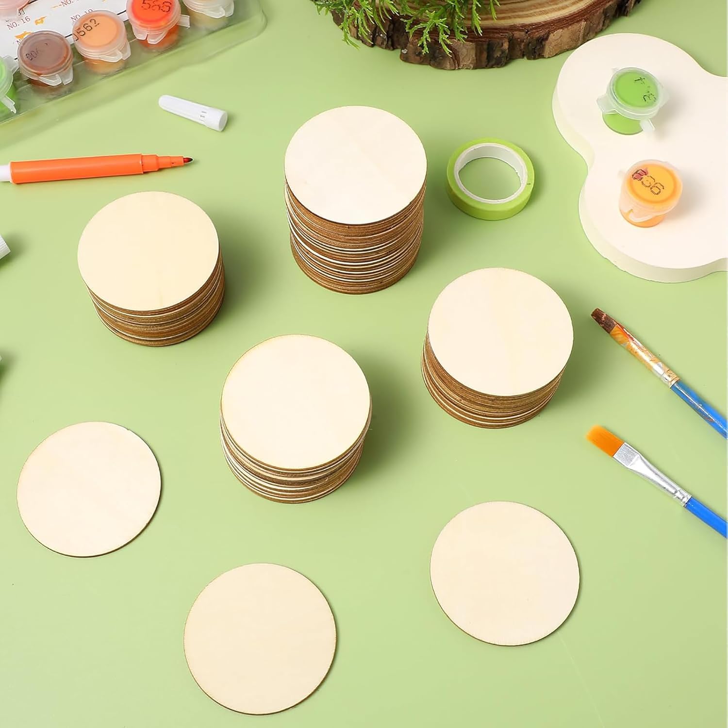 Stacks of round wooden discs on a green surface with painting supplies.
