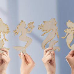 Wooden mermaid ornaments held by hands against a light blue background