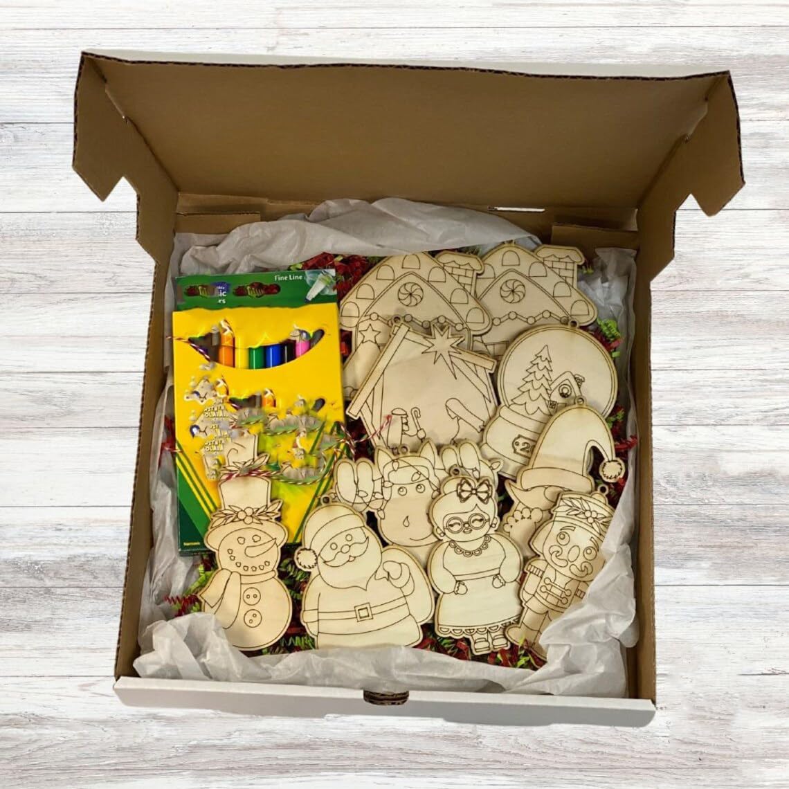 Open box containing wooden Christmas ornaments and coloring books on a wooden surface