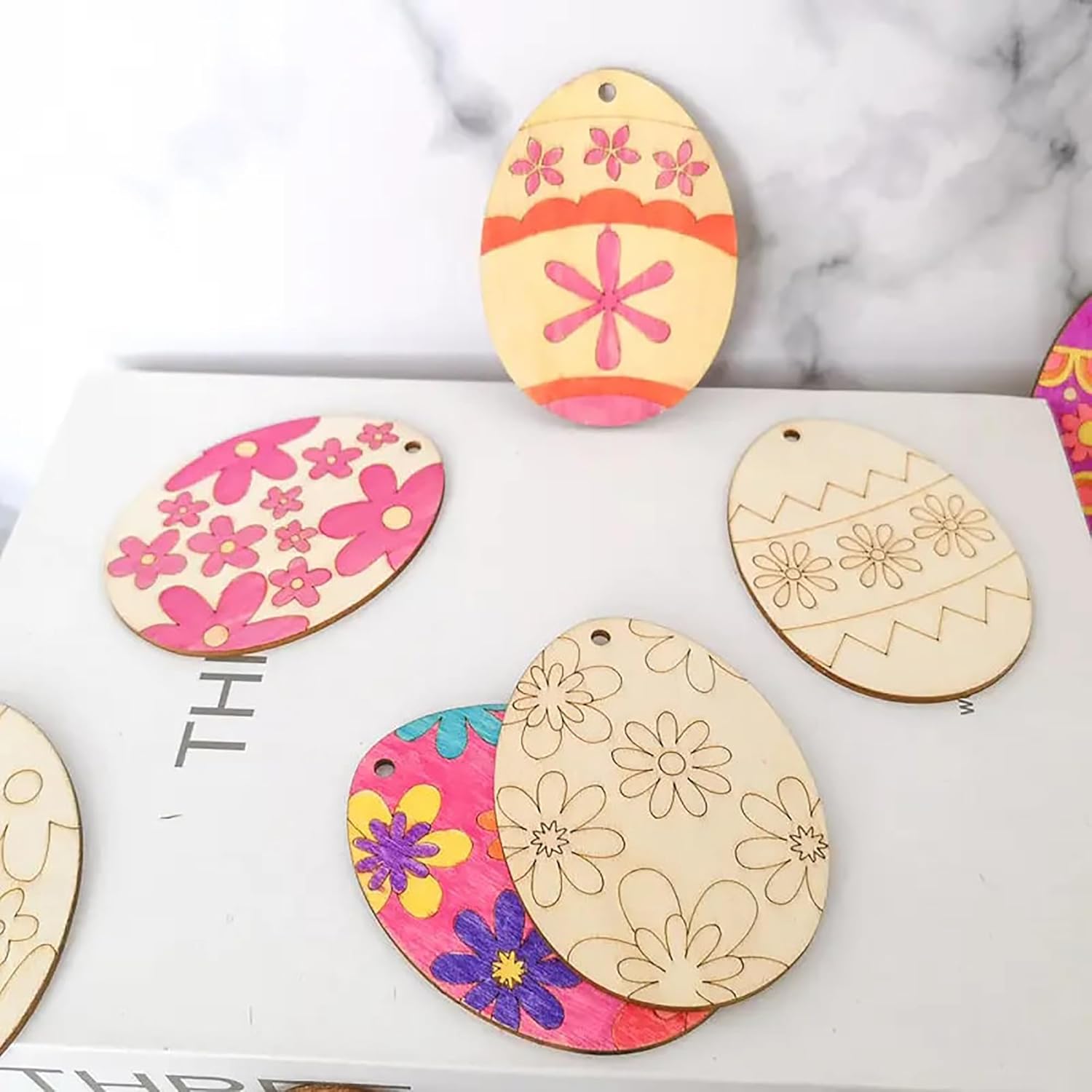 Decorative wooden Easter egg ornaments with floral patterns on a marble surface.