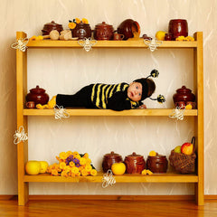 Child in a bee costume lying on a wooden shelf with decorative items.