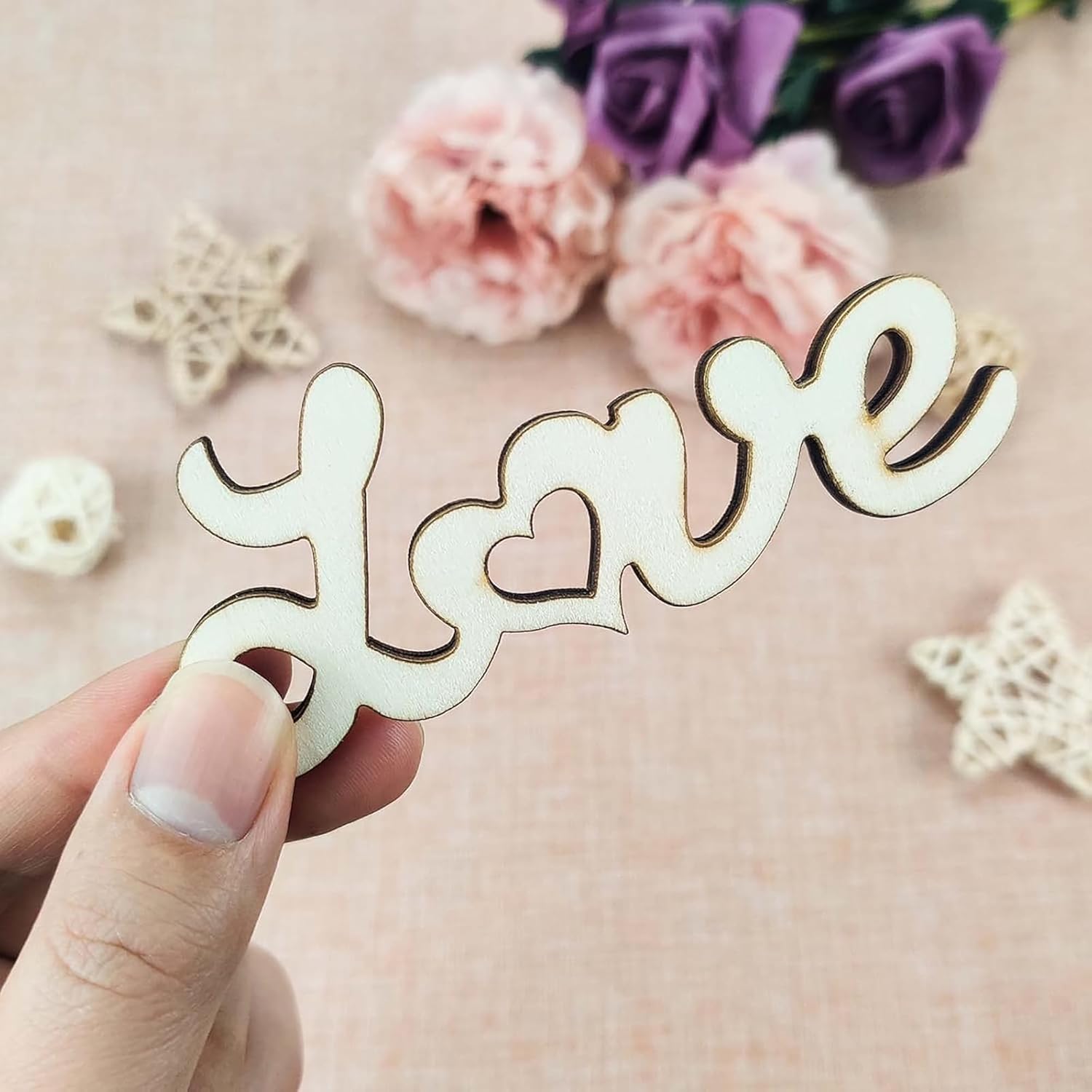 Wooden decorative piece spelling 'love' held by a hand with flowers in the background