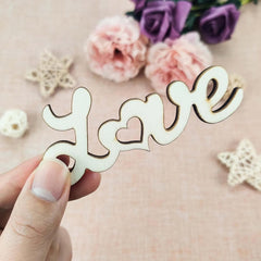 Wooden decorative piece spelling 'love' held by a hand with flowers in the background