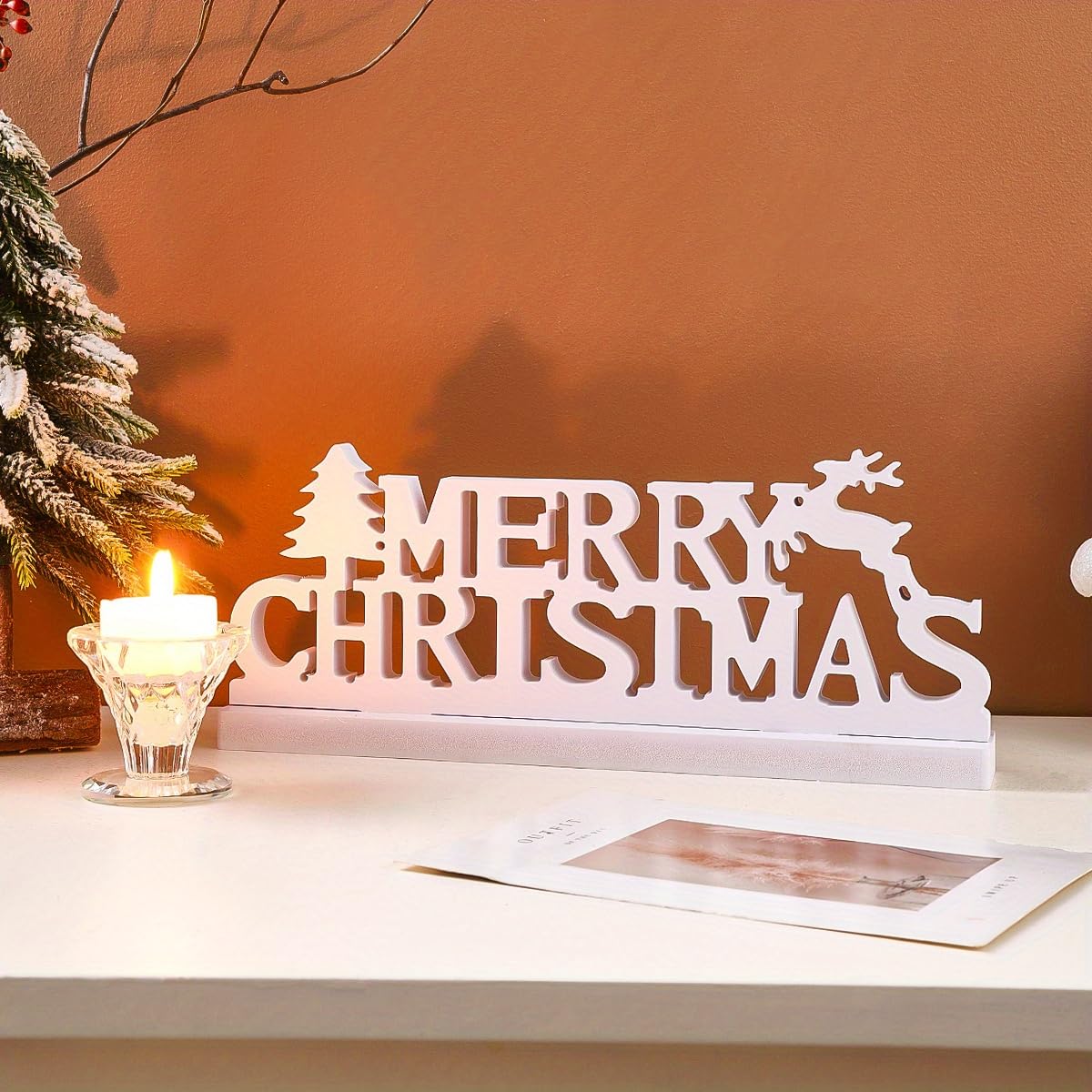Decorative 'Merry Christmas' sign with a candle and card on a table.