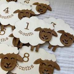 Wooden sheep-shaped age markers with months printed on them, arranged on a textured surface.