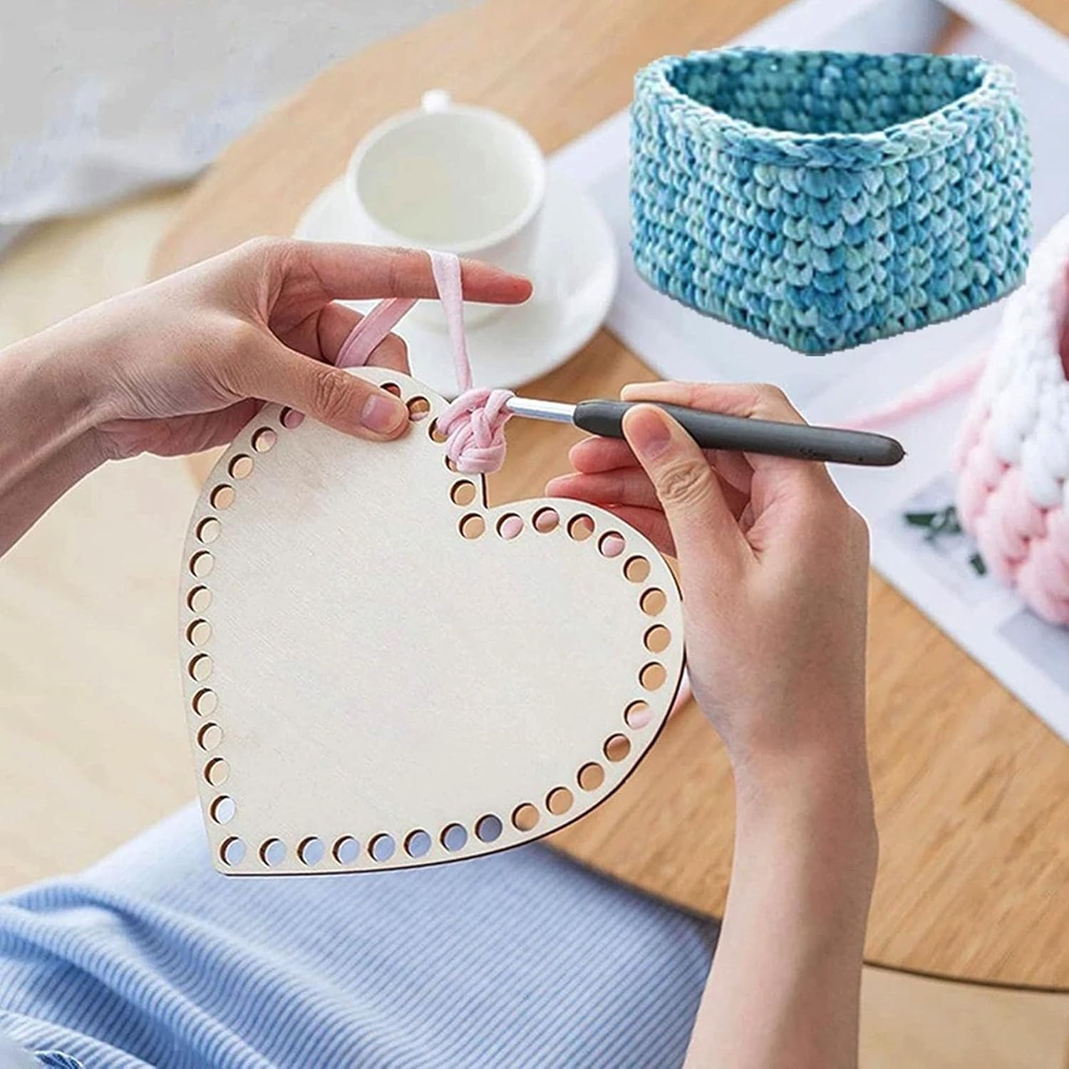 Person using a crochet hook with a heart-shaped wooden tool on a table.