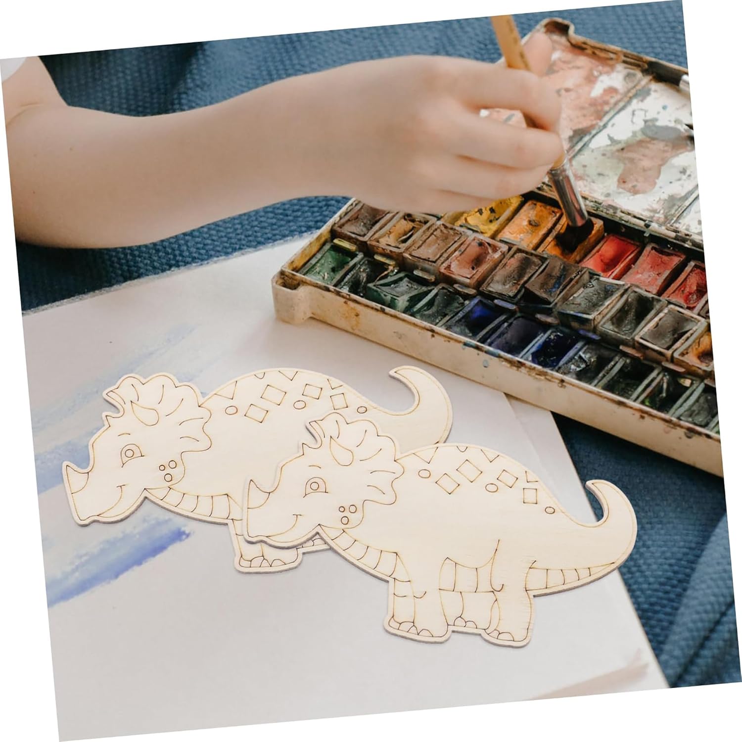 Child painting a dinosaur illustration with watercolors on a white paper.