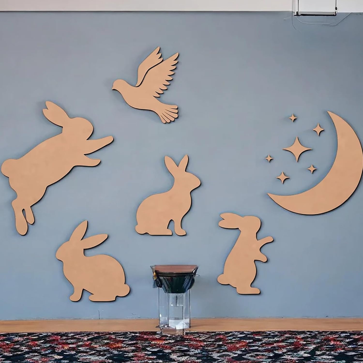 Wooden cutouts of rabbits, a bird, and a moon with stars on a blue wall.