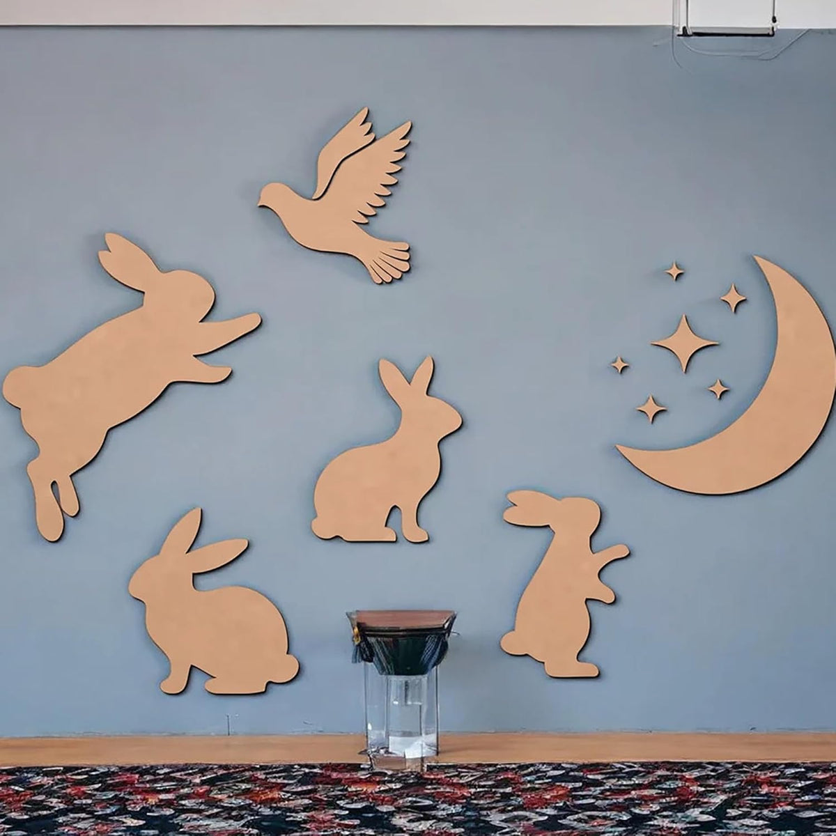 Wooden cutouts of rabbits, a bird, and a moon with stars on a blue wall.