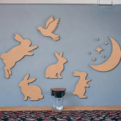 Wooden cutouts of rabbits, a bird, and a moon with stars on a blue wall.