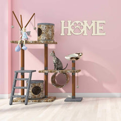 Cat tree with various perches and toys against a pink wall with 'HOME' decor.