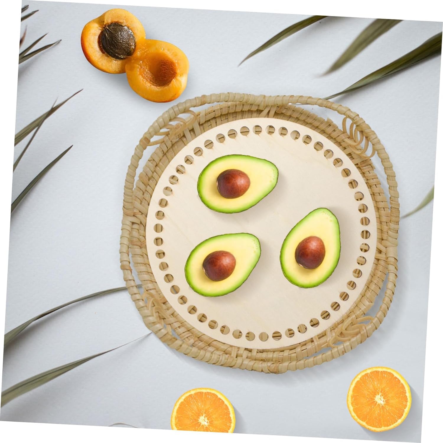 Three avocados on a woven plate with apricots and oranges around on a light background