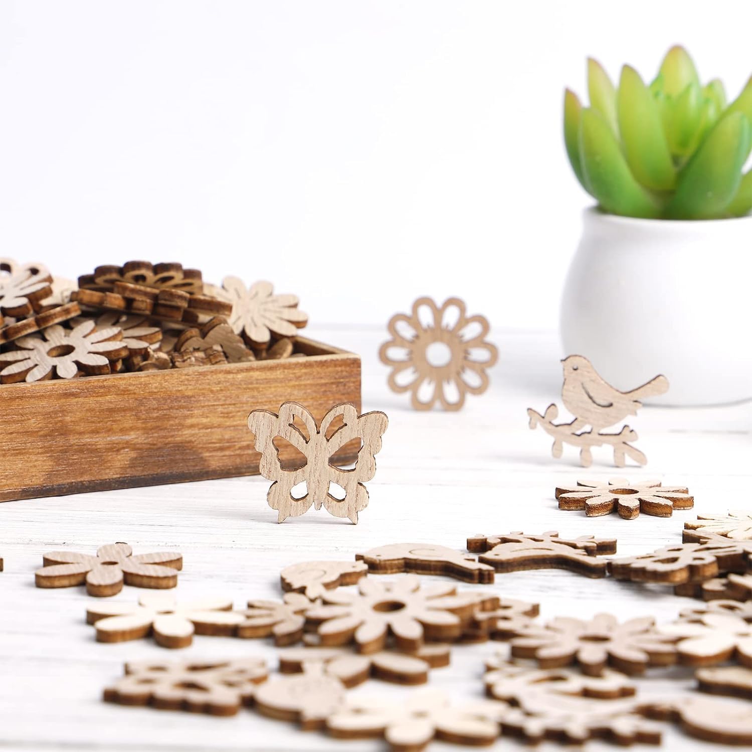Wooden decorative pieces including butterflies, flowers, and birds on a white surface with a potted plant in the background.