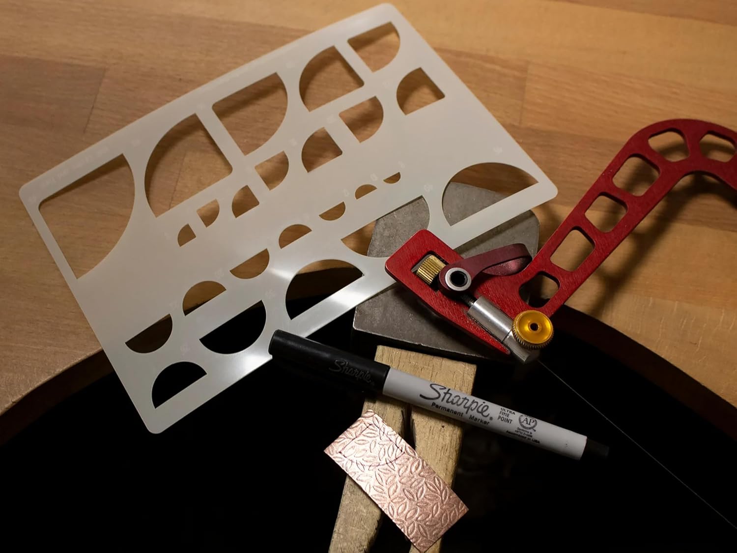 Metal ruler with cut-out shapes on a wooden surface, accompanied by a Sharpie marker.